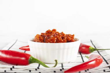 Sıcak ev yapımı harissa ya da acı biber, kimyon, beyaz kareli peçetede beyaz bir cocotte içindeki kişniş sosundan yapılan adjika sosu.