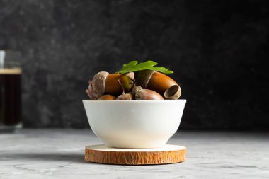 Siyah arka planda beyaz bir tabakta olgun meşe palamutları, kahve çekirdeklerinin alternatifi.