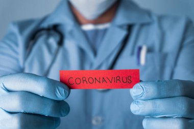 Covid-19 pandemisi. Doktor elinde koronavirüs yazan kırmızı bir kağıt tutuyor..