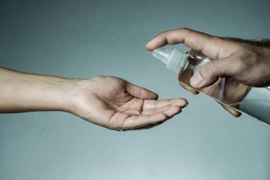 Adam kadının eline dezenfektan püskürtüyor. Covid-19, Coronavirus, SARS-CoV-2 salgını. 2019 - 2020 Roman Coronavirus kavramı ve geçmişi.