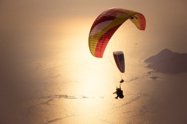 Gökyüzünde paraşütle atlıyor. Paraglider gün batımında dağlarla birlikte denizin üzerinde uçuyor. Oludeniz, Mugla, Türkiye 'de paraglider ve Mavi Göl' ün hava manzarası.