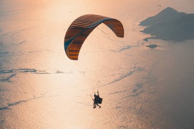Gökyüzünde paraşütle atlıyor. Paraglider gün batımında dağlarla birlikte denizin üzerinde uçuyor. Oludeniz, Mugla, Türkiye 'de paraglider ve Mavi Göl' ün hava manzarası.