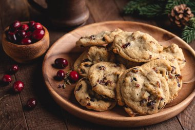 Kızılcık cevizli kurabiyeler, arka planda çam kozalağı ve noel ağacı dalları olan ahşap bir tabakta yığılmıştı.