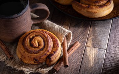 Pişmiş tarçınlı çörek ve tarçın çubuklu bir fincan kahve.