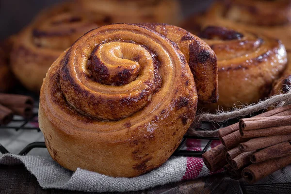 Fresh baked cinnamon buns on a wire rack with cinnamon sticks