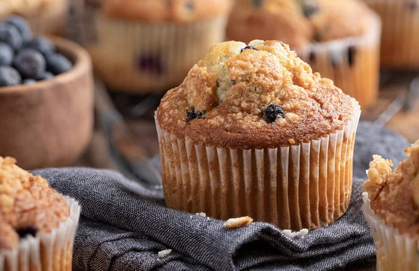 Closeup of a blueberry muffin on a cloth napkin with muffins on a cooling rack in background