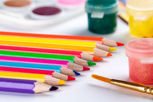 Closeup of school art supplies with colored pencils and paint on a white table