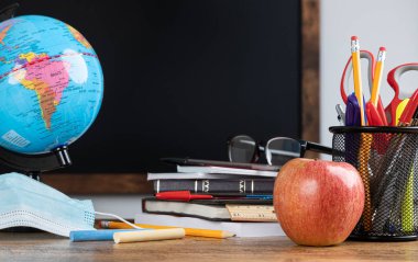 Okul malzemeleri ve arka planda boş tahta olan sınıf masası.