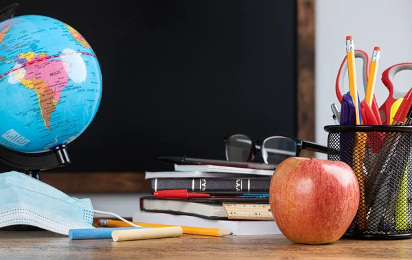 Okul malzemeleri ve arka planda boş tahta olan sınıf masası.