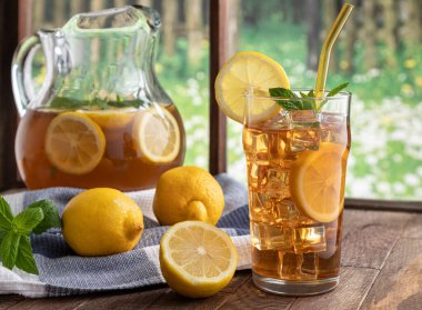 Pencere kenarındaki ahşap masada limonlu ve naneli bir bardak buzlu çay.