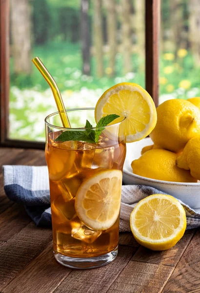 Glass of iced tea and lemon on a wooden table by a window with rural background scene