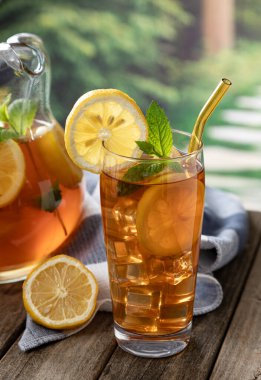 Bir bardak limon dilimli buzlu çay ve kırsal arkaplan manzaralı ahşap bir masada nane.