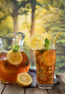 Bir bardak limon dilimli buzlu çay ve kırsal arkaplan manzaralı ahşap bir masada nane.