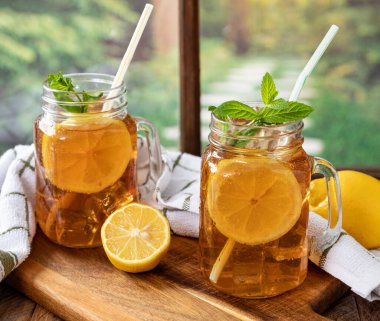 İki bardak buzlu çay, limon ve naneli. Arka planda kırsal bir pencere var.