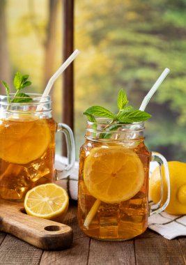 İki bardak buzlu çay, limon ve naneli. Arka planda kırsal bir pencere var.