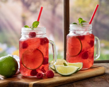 İki bardak yabanmersini suyu, ahududu ve kireç. Kırsal arka plan manzaralı bir pencerenin yanında.