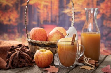 Kırsal bir ahşap masada sonbahar arkaplanlı cam elma suyu ve taze elmalar.