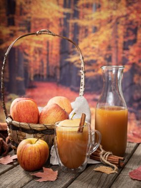 Kırsal bir ahşap masada sonbahar arkaplanlı cam elma suyu ve taze elmalar.