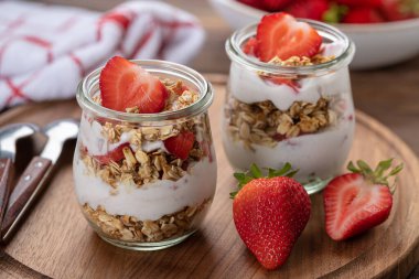 Çilekli yoğurt ve ahşap tabakta taze çilekli granola parfe.