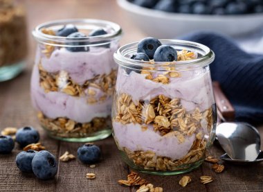 Tahta bir masada yabanmersinli yoğurt ve taze yaban mersinli granola parfe.
