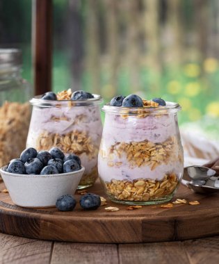 Yaban mersinli yoğurtlu granola parfe ve kırsal arka planı olan bir pencerenin yanındaki ahşap tabakta taze yaban mersini.