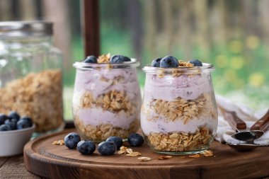 Yaban mersinli yoğurtlu granola parfe ve kırsal arka planı olan bir pencerenin yanındaki ahşap tabakta taze yaban mersini.