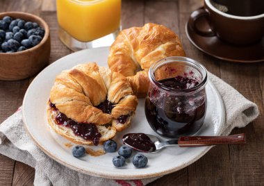 Kruvasan, yabanmersini ve böğürtlen reçeli bir tabakta portakal suyu ve kahve.