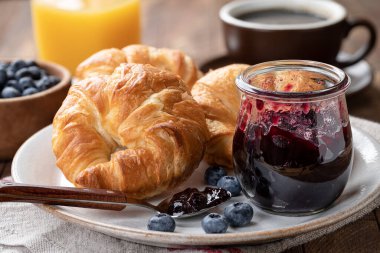 Yabanmersini reçelli kruvasan ve meyve suyu ve kahve dolu bir tabakta yaban mersini.