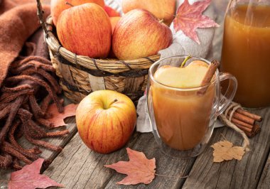 Elma şarabı, battaniyeli taze elmalar ve kırsal bir ahşap masada sonbahar yaprakları.