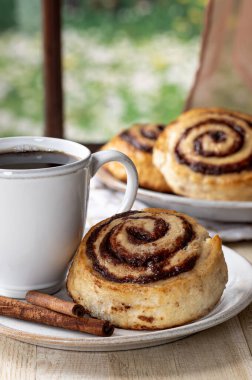 Camdan yapılmış tarçınlı çörek ve bir fincan kahve.