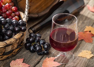 Üzümlü kırmızı şarap, şarap şişesi ve sonbahar yapraklı ahşap masa üzerinde varil.