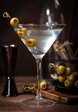 Bambu kazmalı zeytinli martini kokteyli ve koyu ahşap arka planda kâse.