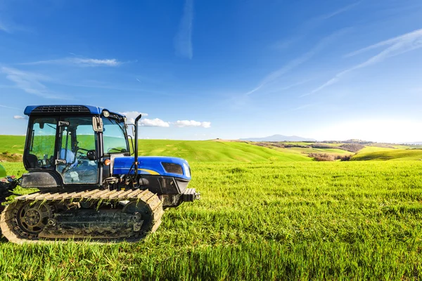 Tractor on tracks in the summer sunny day on a green field. — Stock Photo, Image