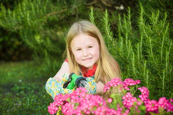 Hermosa chica rubia regando flores, césped en una hermosa soleada —  Fotos de Stock