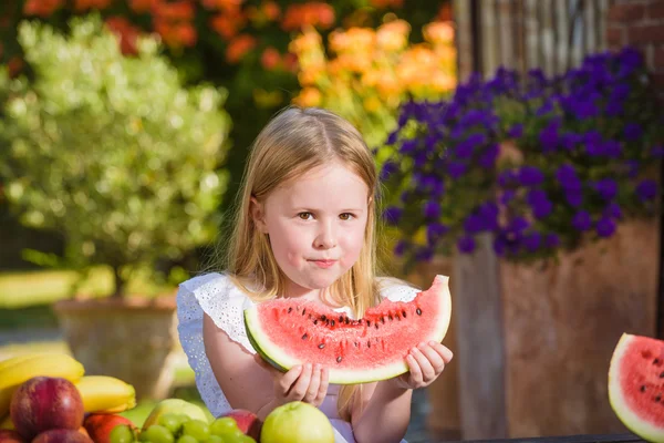 Šťastná dívka s velkým červeným dílek melounu sedí na rustikální ta — Stock fotografie
