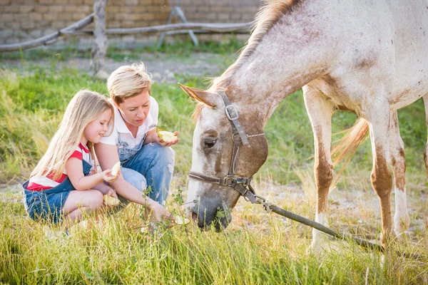 Mère et fille nourrissant un cheval d'une pomme dans le haras . — Photo