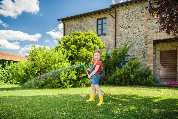 Beautiful blond girl watering flowers, lawn on a sunny beautiful day in front of the house. — Stock Photo, Image