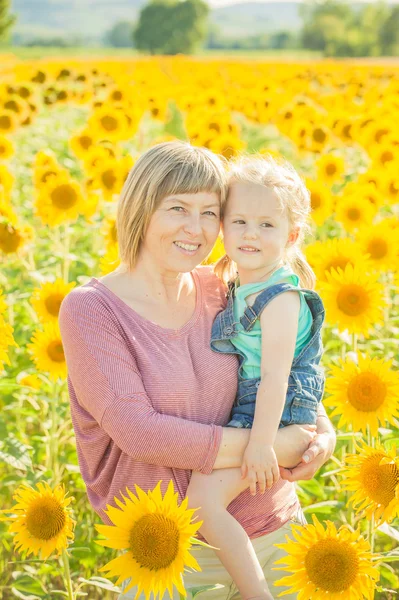 Mom with daughter in between beautiful sunflowers in summer day. — Stock Photo, Image