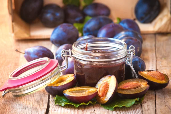 Vaso di marmellata di prugne circondato da prugne su sfondo in legno rurale t — Foto Stock