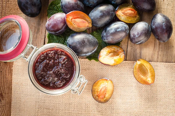 Vaso di marmellata di prugne circondato da prugne su sfondo in legno rurale t — Foto Stock