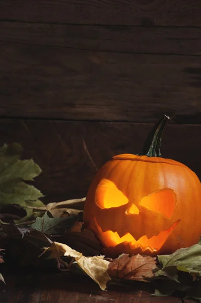 Abóbora de Halloween com olhos brilhantes e dentes nas folhas com — Fotografia de Stock