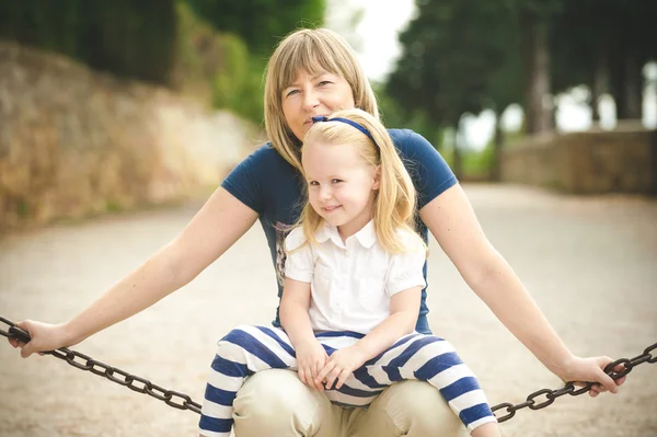 Rubia madre e hija en el parque, sentadas en una cadena — Foto de Stock