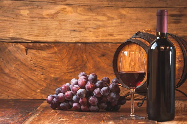 Uve rosse e una bottiglia di vino e botte su tavola rustica di legno — Foto Stock
