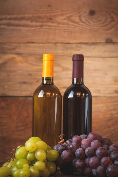 Červené a bílé víno láhev s hrozny na dřevěný rustikální stůl. — Stock fotografie