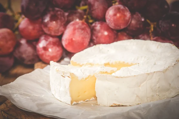 Stinkende camembert kaas op een rustieke houten tafel met druiven — Stockfoto