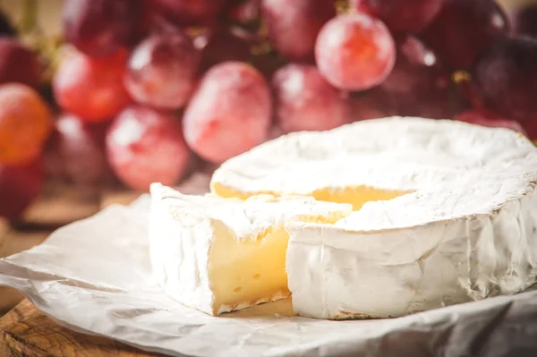 Queso camembert apestoso sobre una mesa rústica de madera con uvas —  Fotos de Stock