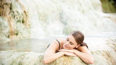 Pretty young woman takes a bath in the natural thermal waters of clipart