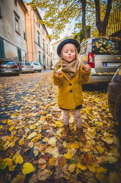 Niña juega con hojas amarillas bajo el sol de otoño . — Foto de Stock
