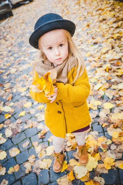 Niña juega con hojas amarillas bajo el sol de otoño . — Foto de Stock