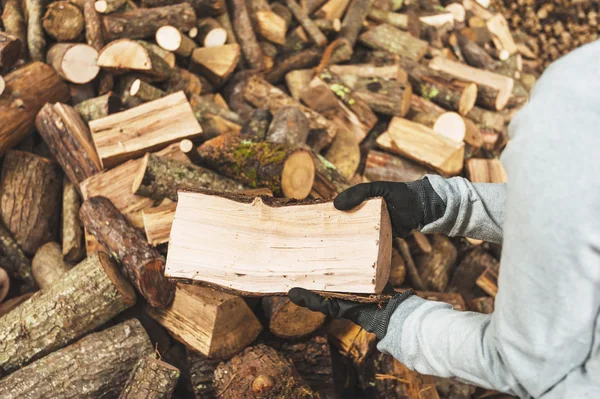 Ved i en träbit lagras i stacken, händer som håller en — Stockfoto